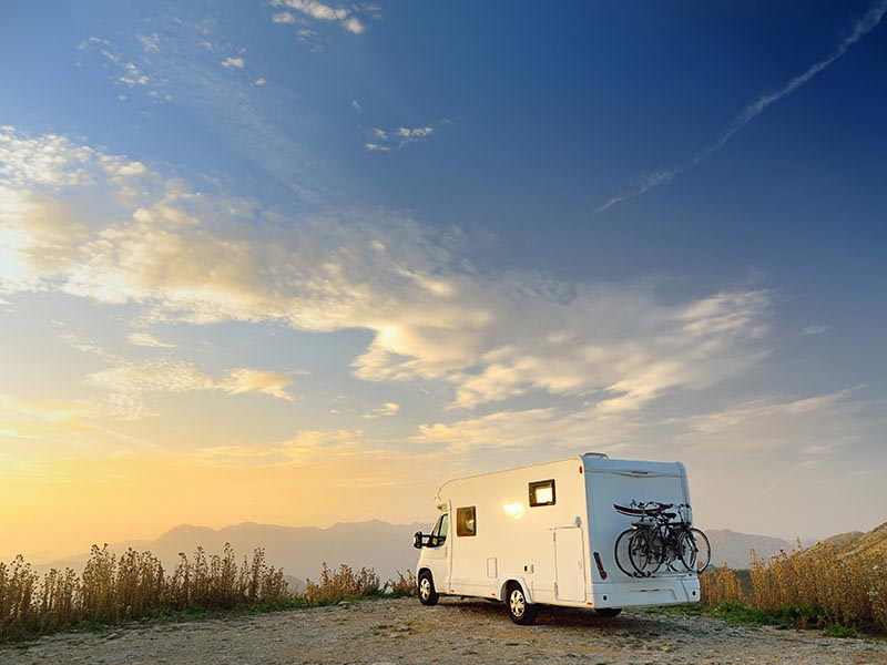 Campervan parked on a hill at sunset with bicycles mounted on the back overlooking a mountain landscape