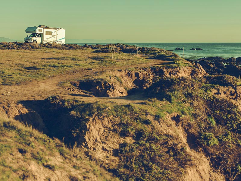 Campervan parked near a coastal cliff with visible ground erosion overlooking the sea.